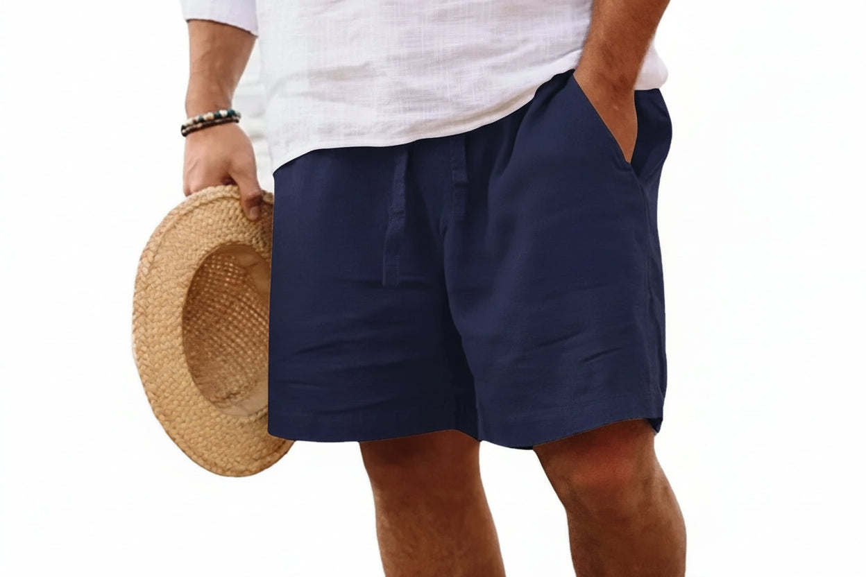 Person wearing navy shorts holding a straw hat on a white background
